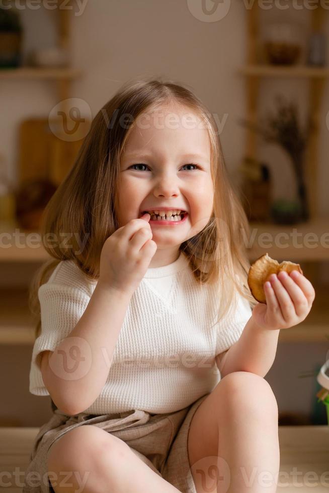 süß wenig Mädchen isst natürlich Pastille beim Zuhause im ein hölzern Küche. Essen zum Kinder von natürlich Produkte foto