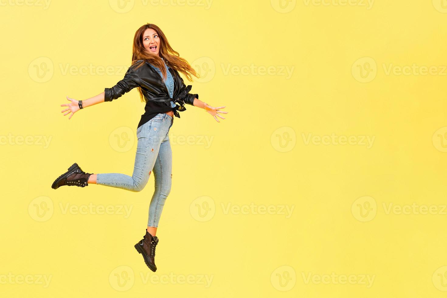 Gelb Hintergrund, ein Mädchen im ein Leder Jacke im das Stil von Felsen, zeigt an Emotionen, kostenlos Raum zum Text, springt foto