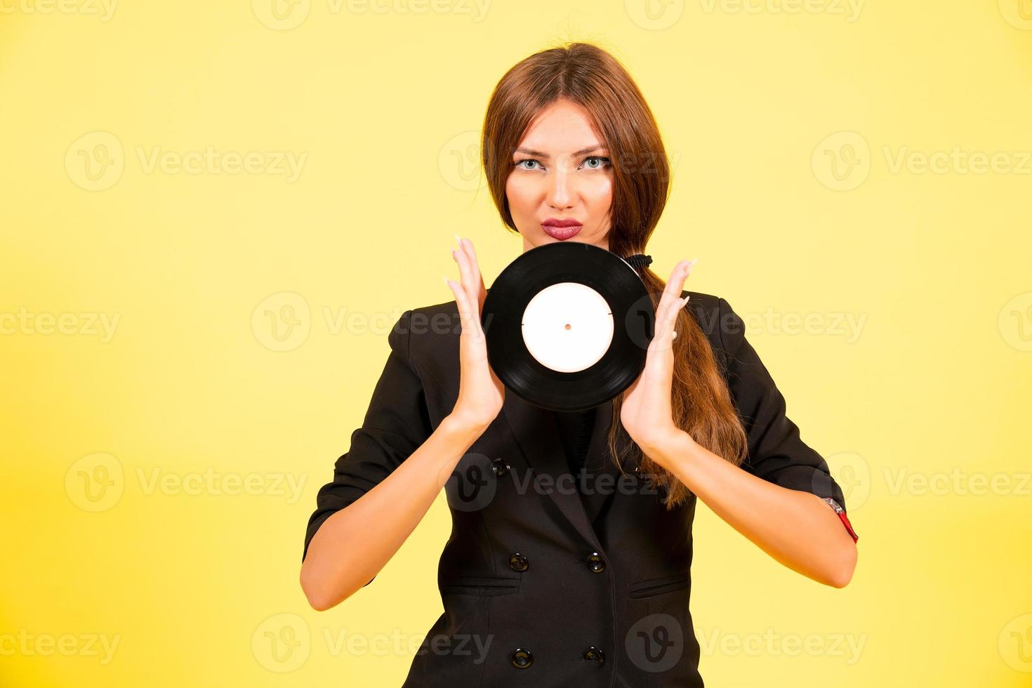 Mädchen im ein schwarz passen auf ein Gelb Hintergrund mit ein Aufzeichnung im ihr Hände, Musik, das Mädchen zeigt an Emotionen foto