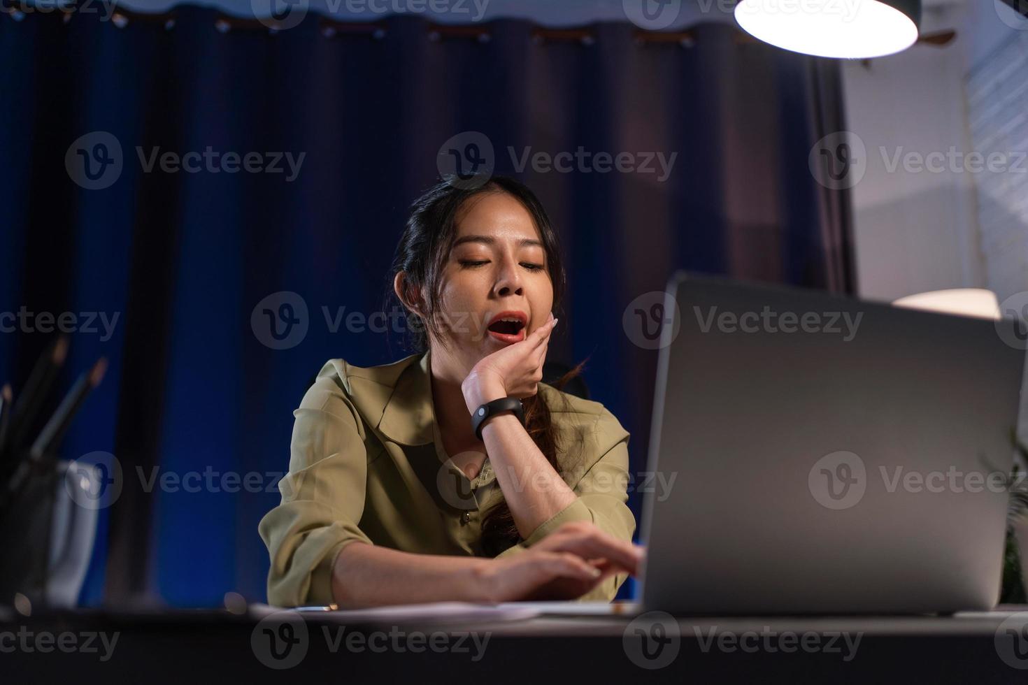 asiatisch Frau Gefühl schläfrig und Arbeit mit Laptop Computer beim Nacht, Arbeiten Überlast. foto