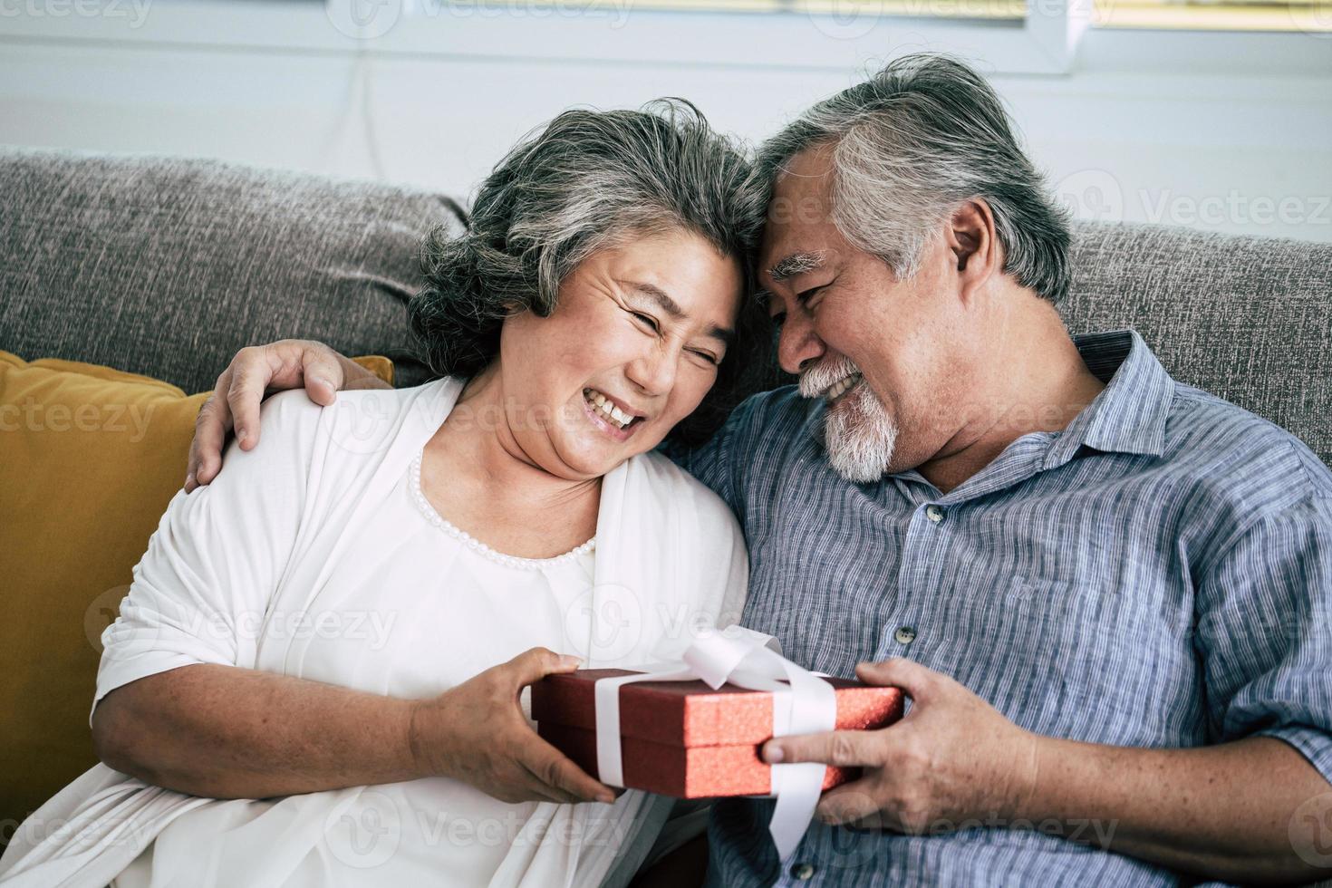 älteres Ehepaar überrascht mit Geschenkbox im Wohnzimmer foto