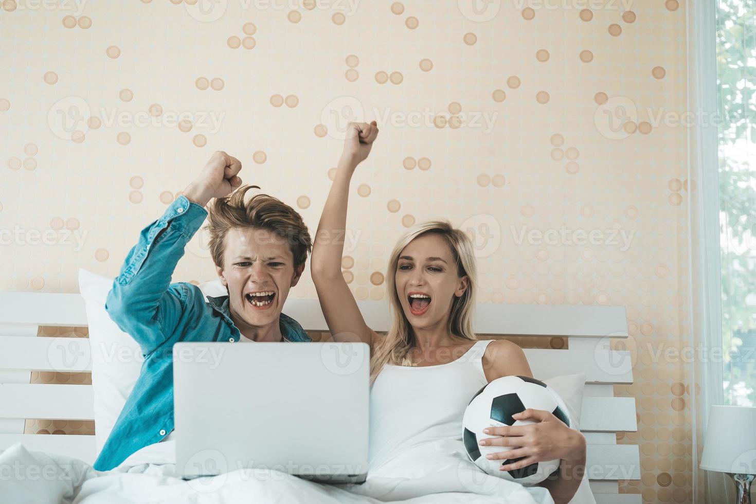 glückliches Paar, das Fußball auf dem Bett sieht foto