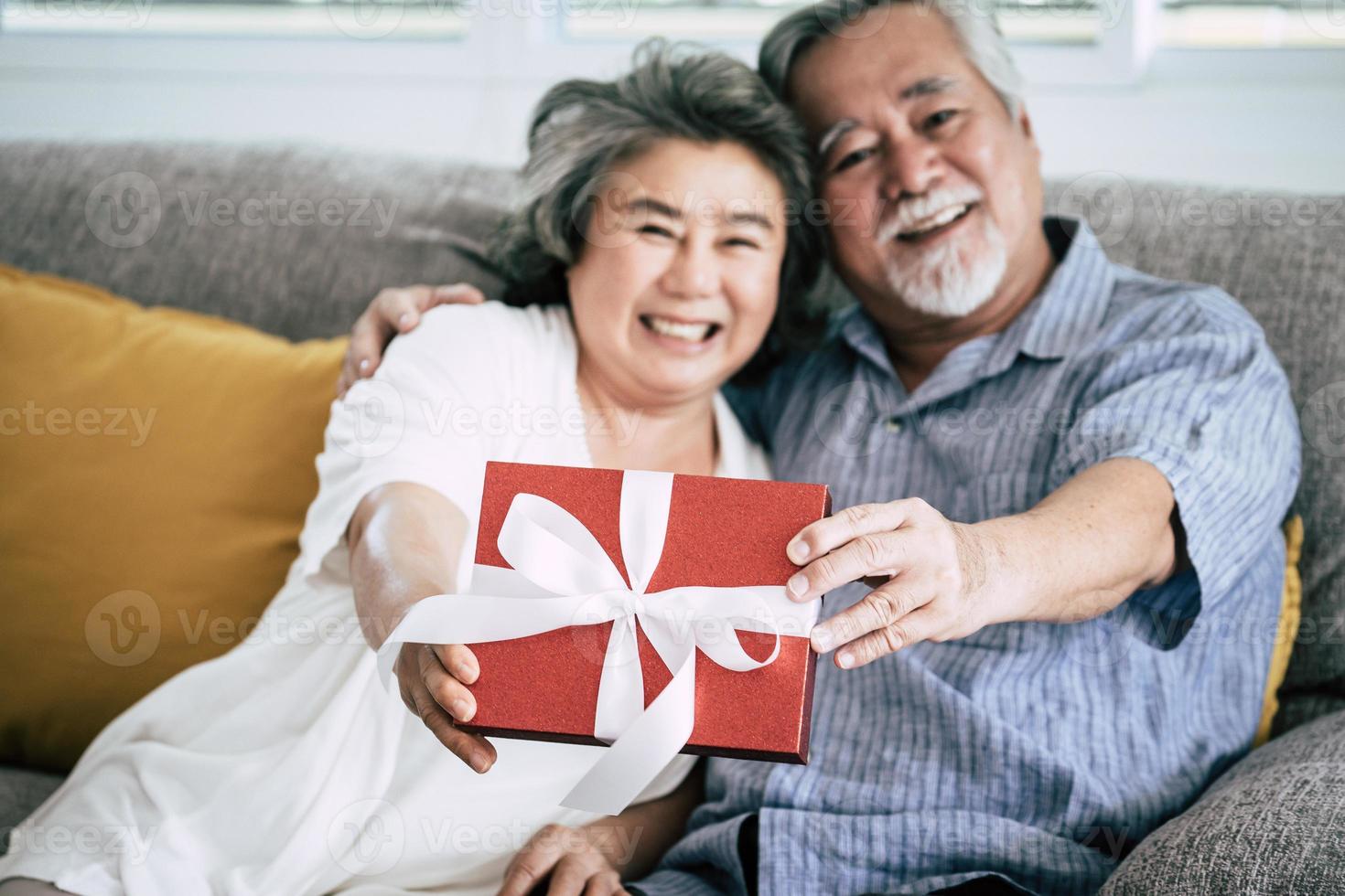 älteres Ehepaar überrascht mit Geschenkbox im Wohnzimmer foto