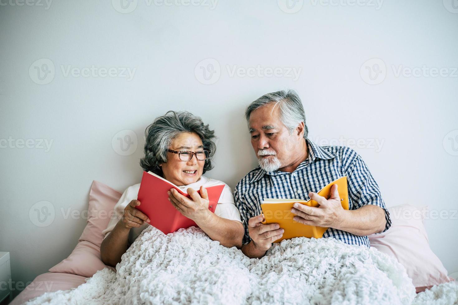 älteres Ehepaar, das auf dem Bett liegt und ein Buch liest foto