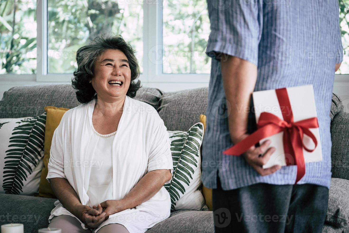 älteres Ehepaar überrascht mit Geschenkbox im Wohnzimmer foto