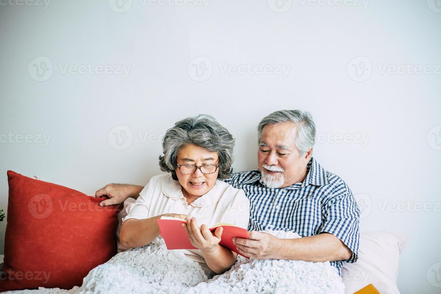 älteres Ehepaar, das auf dem Bett liegt und ein Buch liest foto