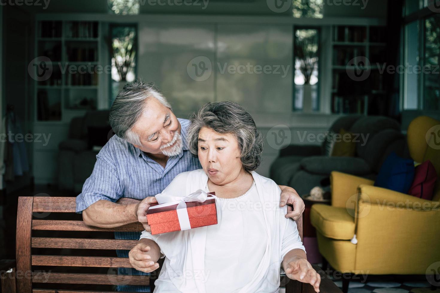 lächelnder älterer Ehemann, der Überraschung macht und seiner Frau Geschenkbox gibt foto