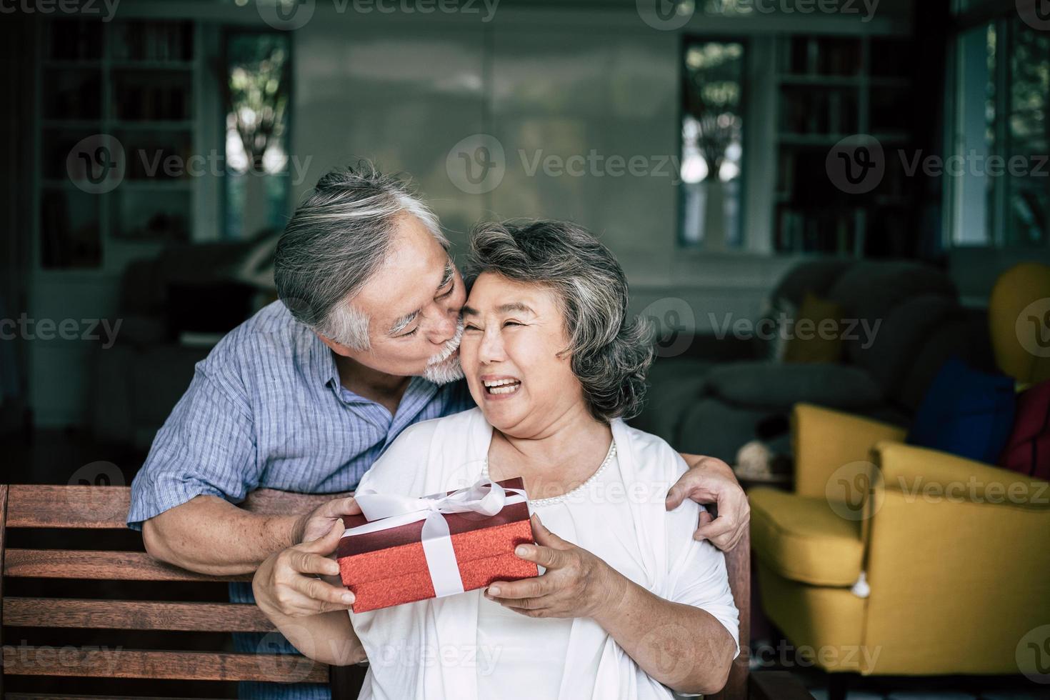 lächelnder älterer Ehemann, der Überraschung macht und seiner Frau Geschenkbox gibt foto