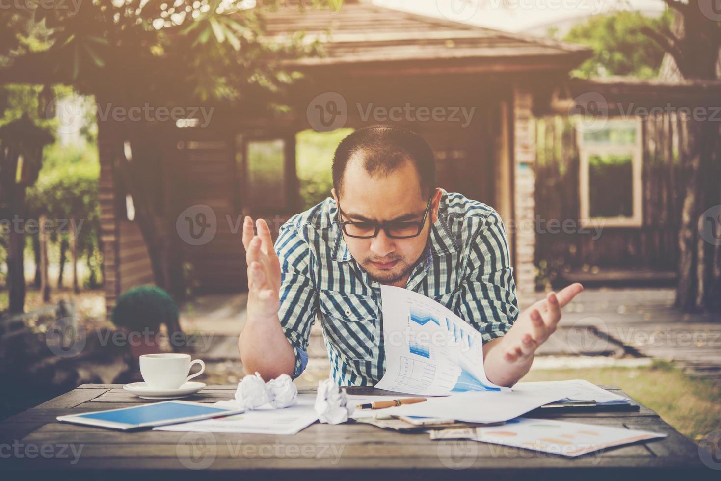 gestresster Geschäftsmann mit Papieren und Diagrammen, die zu Hause am Tisch sitzen foto