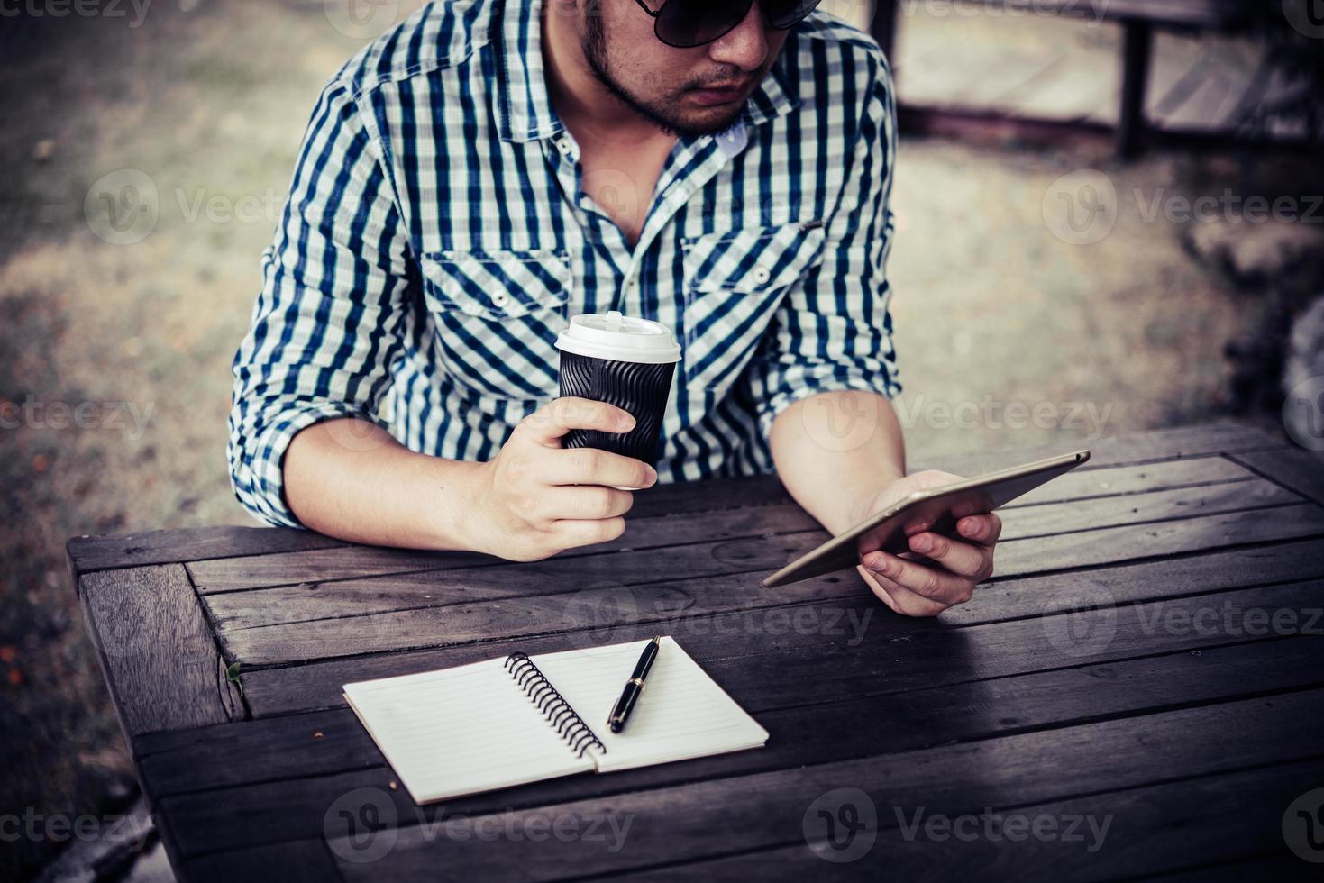 junger Mann, der digitale Tablette beim Kaffeetrinken im Hausgarten verwendet foto