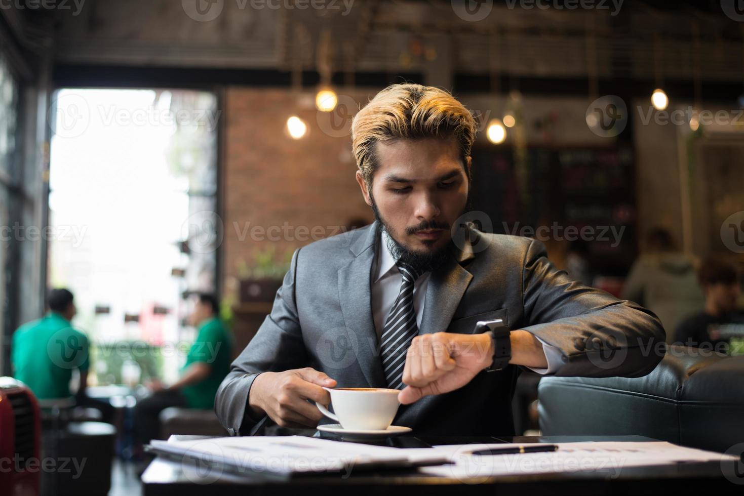 Geschäftsmann, der auf seine Uhr schaut, während er im Café arbeitet foto