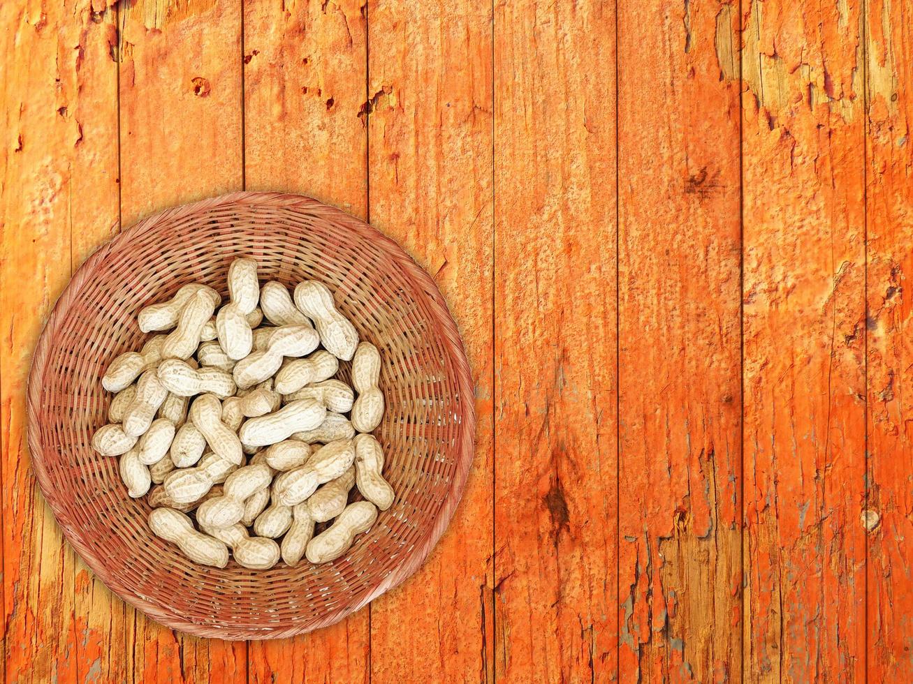 Erdnüsse im Weidenkorb auf Holztischhintergrund foto
