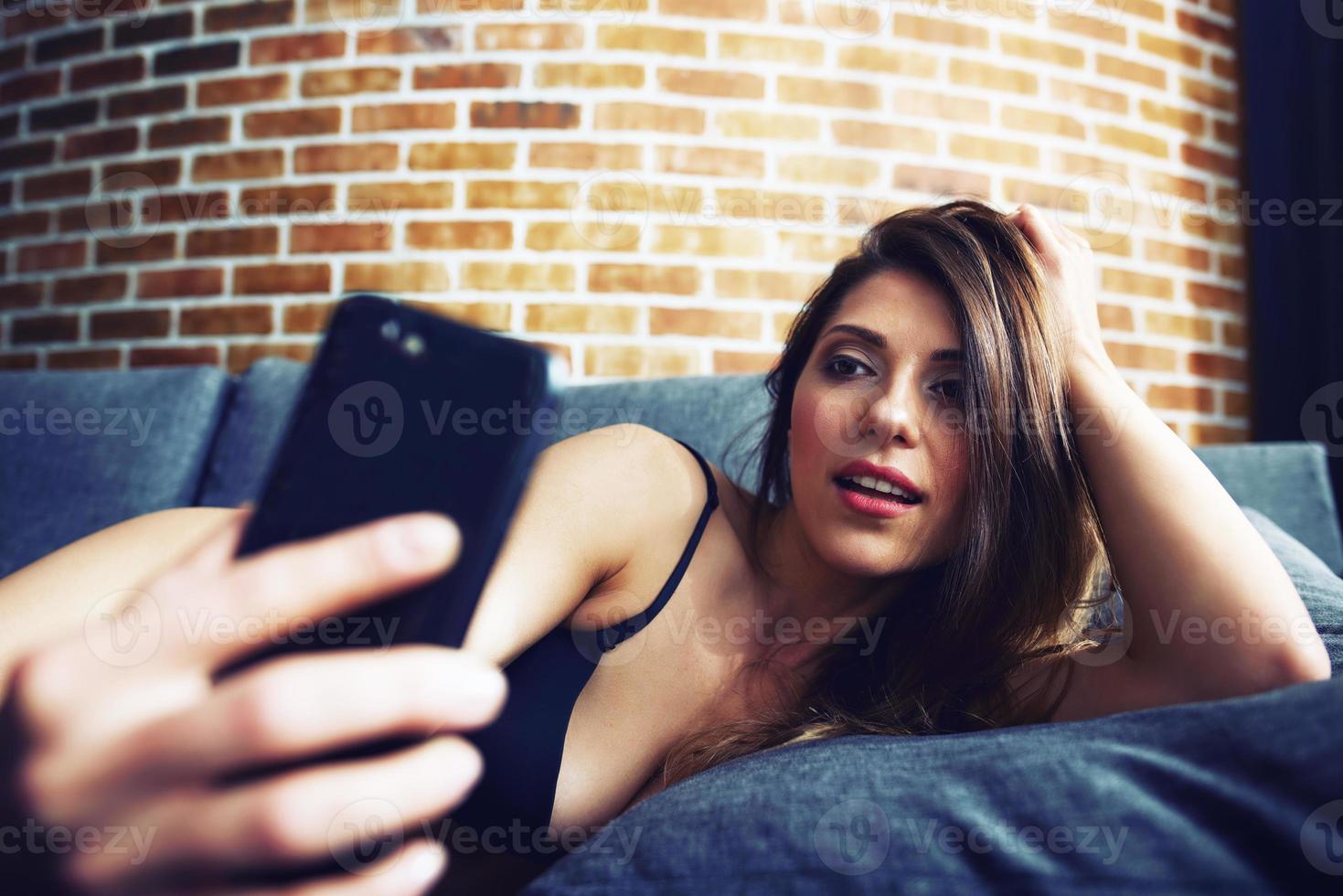 Brünette Mädchen schießt ein Selfie mit Smartphone auf Sofa im Dessous foto