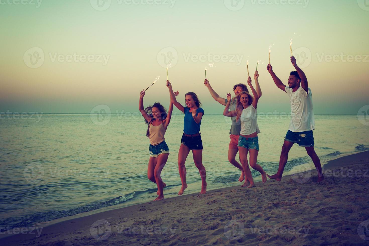 glücklich lächelnd freunde Laufen beim das Strand mit funkelnd Kerzen foto