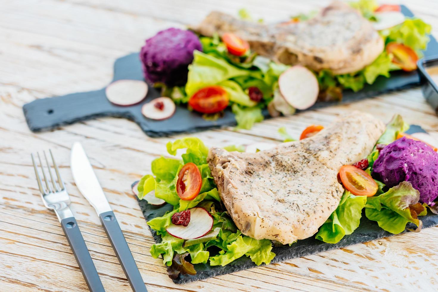 Gegrilltes Grill-Schweinekotelett-Fleischsteak auf schwarzem Teller mit Gemüse foto