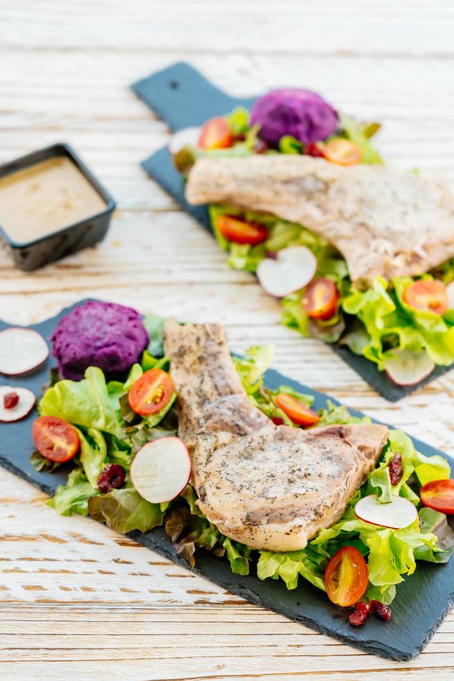 Gegrilltes Grill-Schweinekotelett-Fleischsteak auf schwarzem Teller mit Gemüse foto