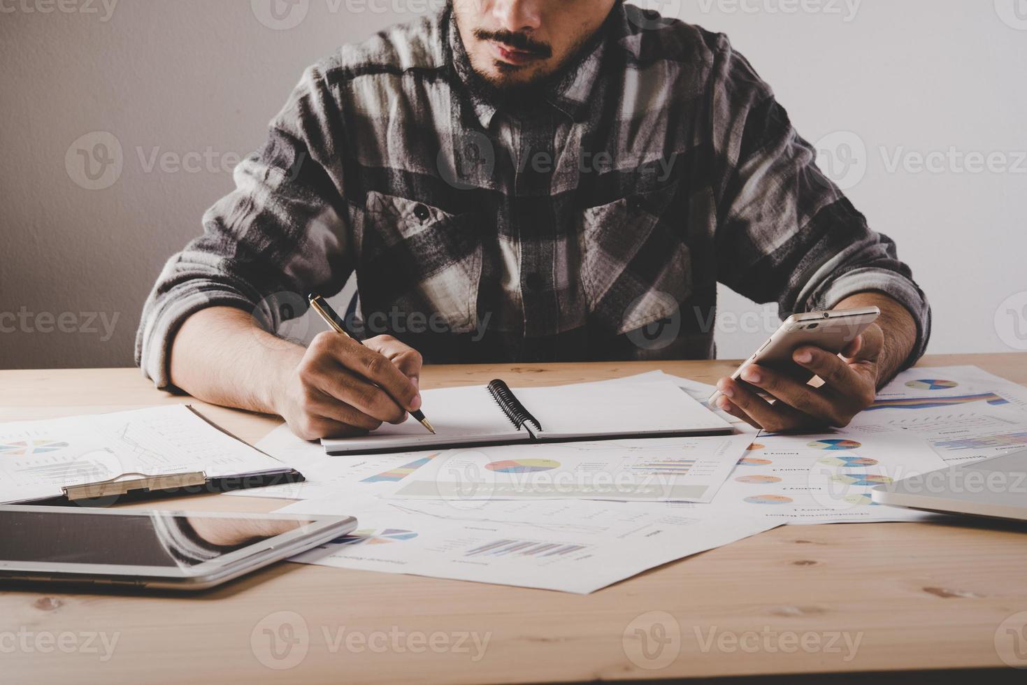 junger Geschäftsmann schreibt in ein Notizbuch, während er Geschäftsdaten im Büro analysiert foto