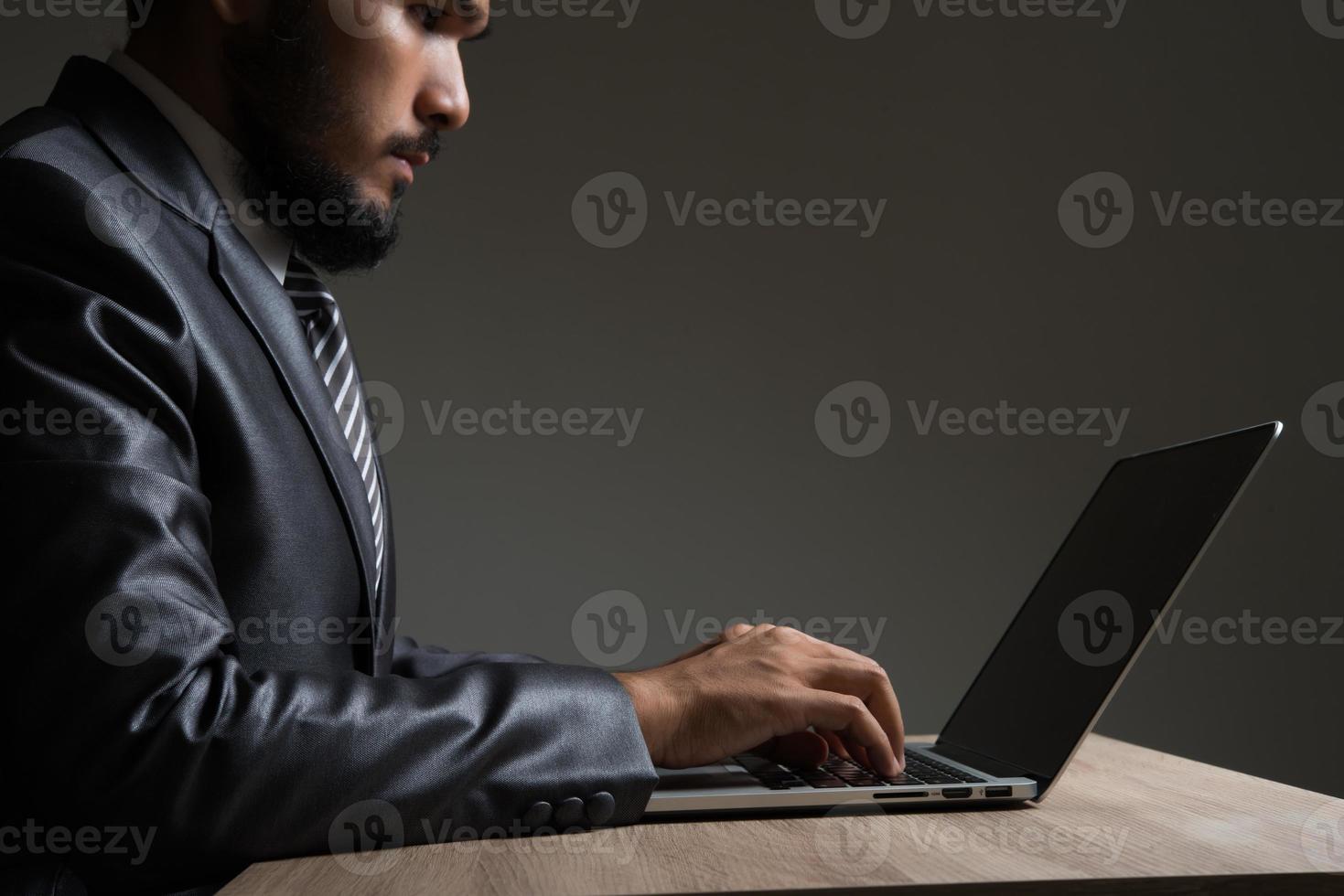 junger Geschäftsmann sitzt arbeitend mit Laptop lokalisiert auf schwarzem Hintergrund foto