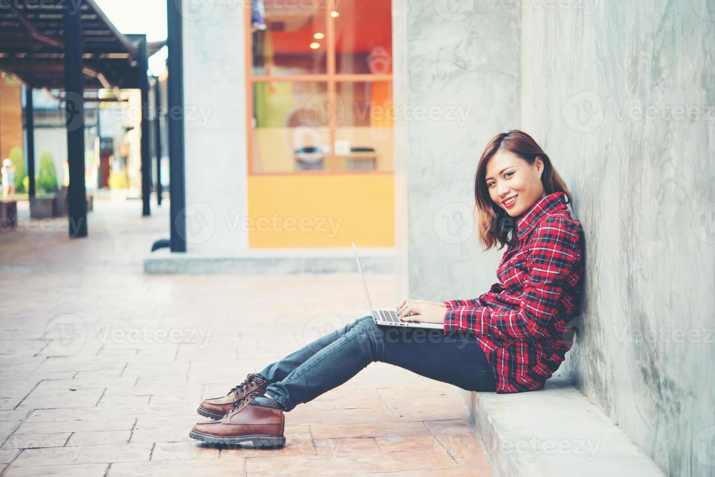 glückliche junge Hipsterfrau, die ihren Laptop benutzt, während sie auf dem Boden sitzt foto