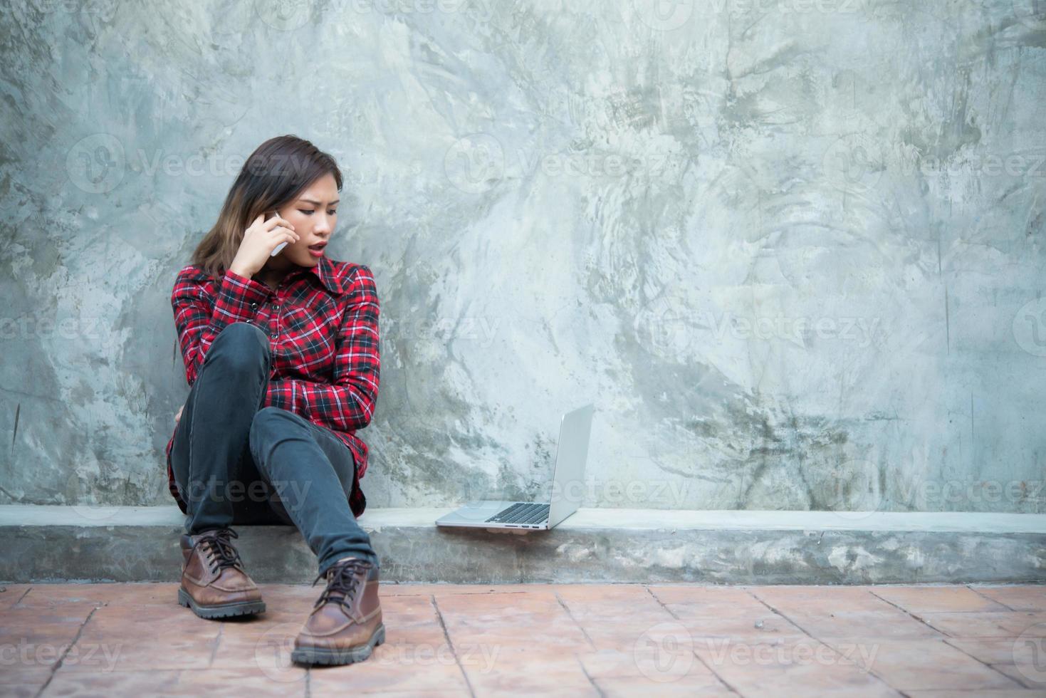 junge Hipsterfrau im coolen Outfit, die auf dem Boden sitzt und am Telefon spricht foto