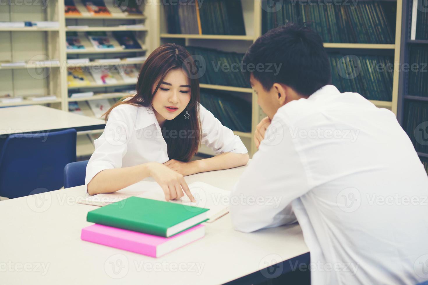 junges asiatisches Studentenpaar in der Bibliothek, das zusammen ein Buch liest foto