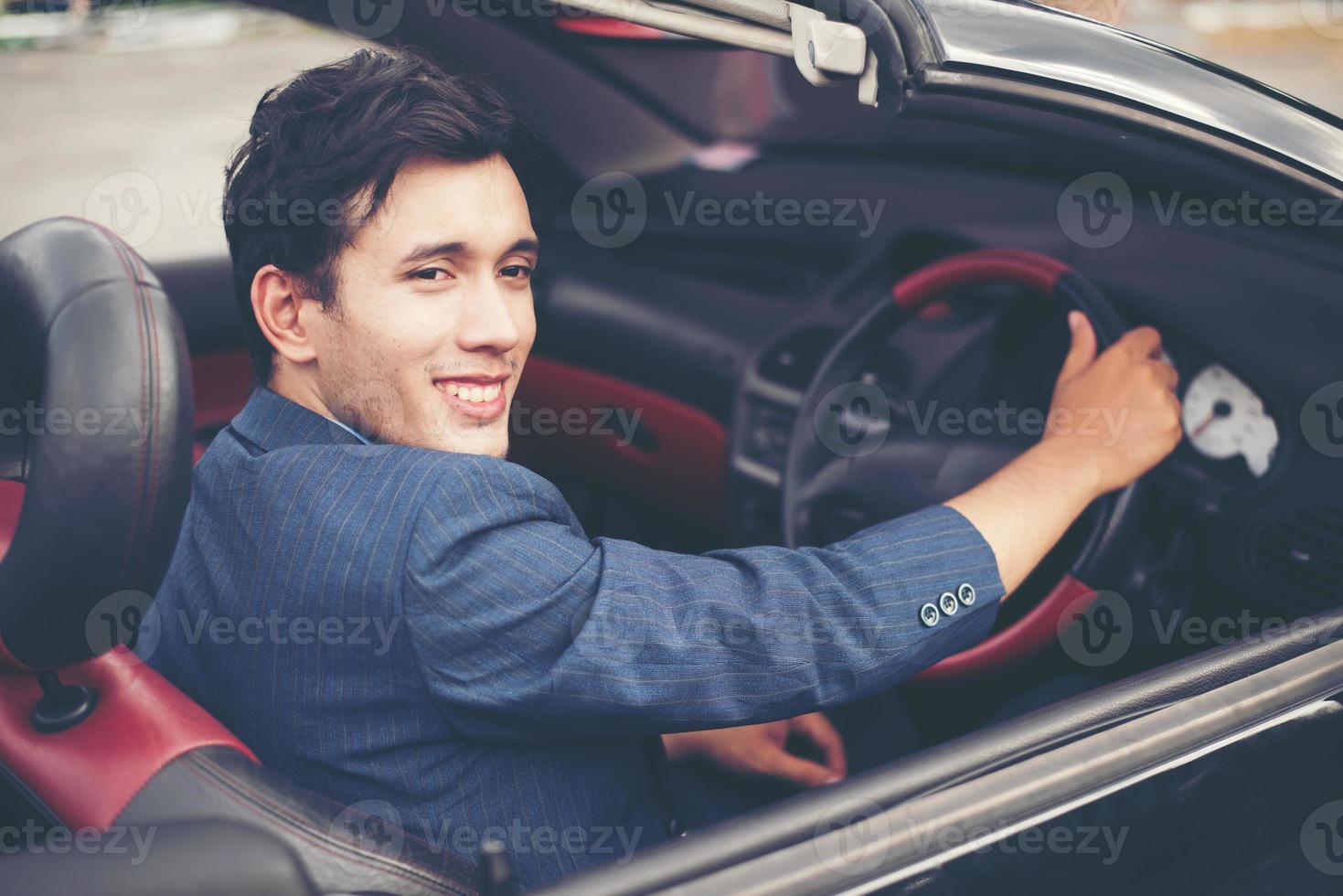 schöner junger Mann im Sportwagen, der einen Anzug trägt foto