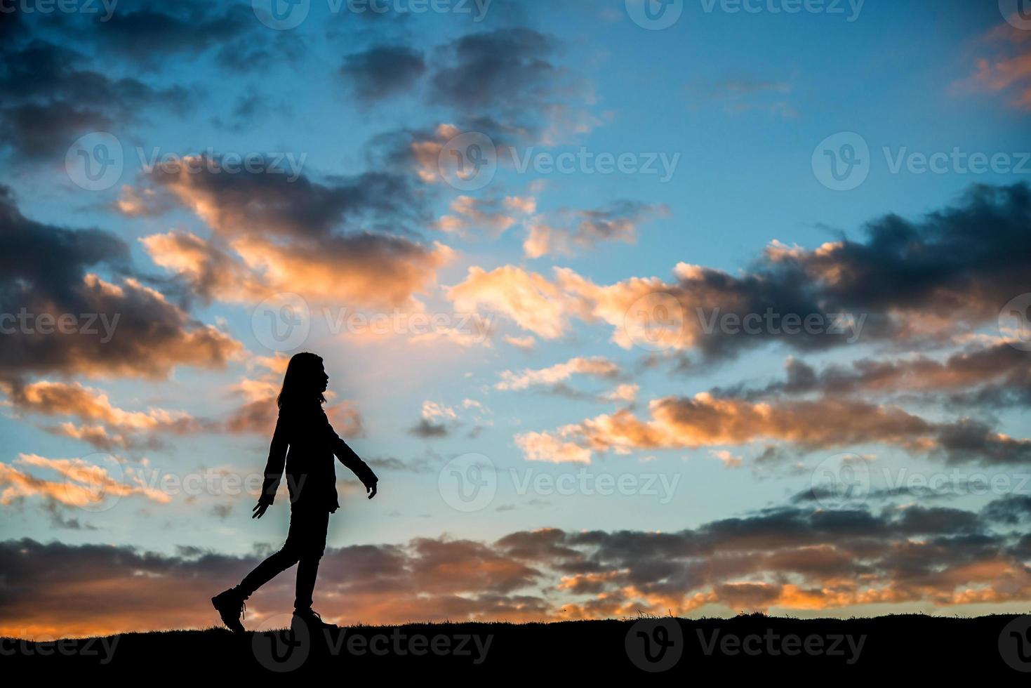 Silhouette einer Frau, die bei Sonnenuntergang geht foto