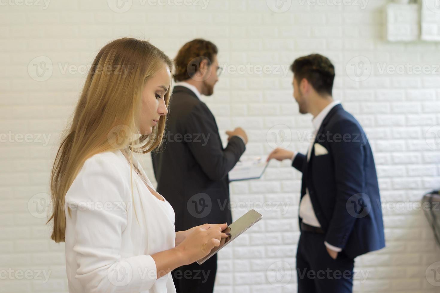 Geschäftsfrau, die digitales Tablett verwendet, während Mitarbeiter im Hintergrund interagieren foto
