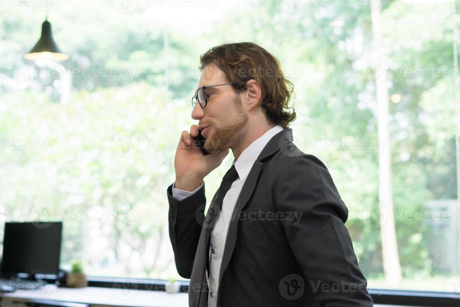 junger Geschäftsmann, der Smartphone beim Stehen im Büro verwendet foto