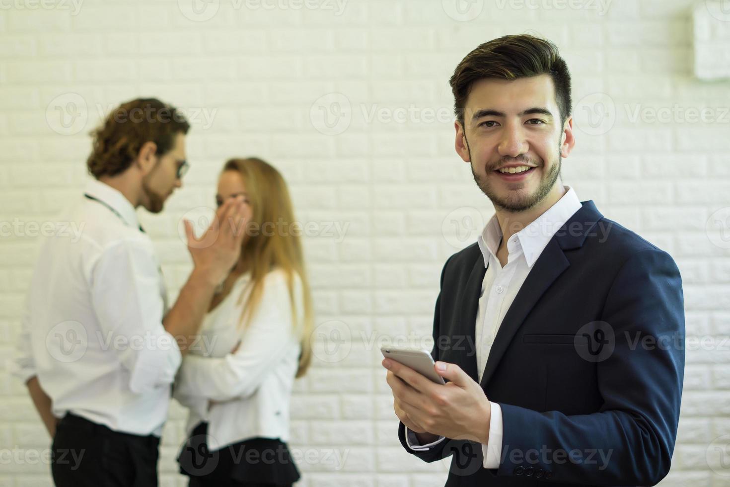 Geschäftsmann mit Smartphone, während Mitarbeiter im Hintergrund interagieren foto