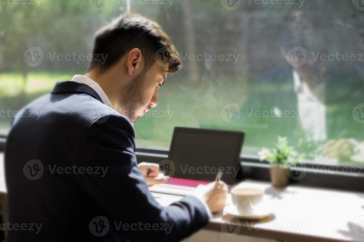 junger Geschäftsmann, der einen Anzug trägt und Laptop in einem Café benutzt foto