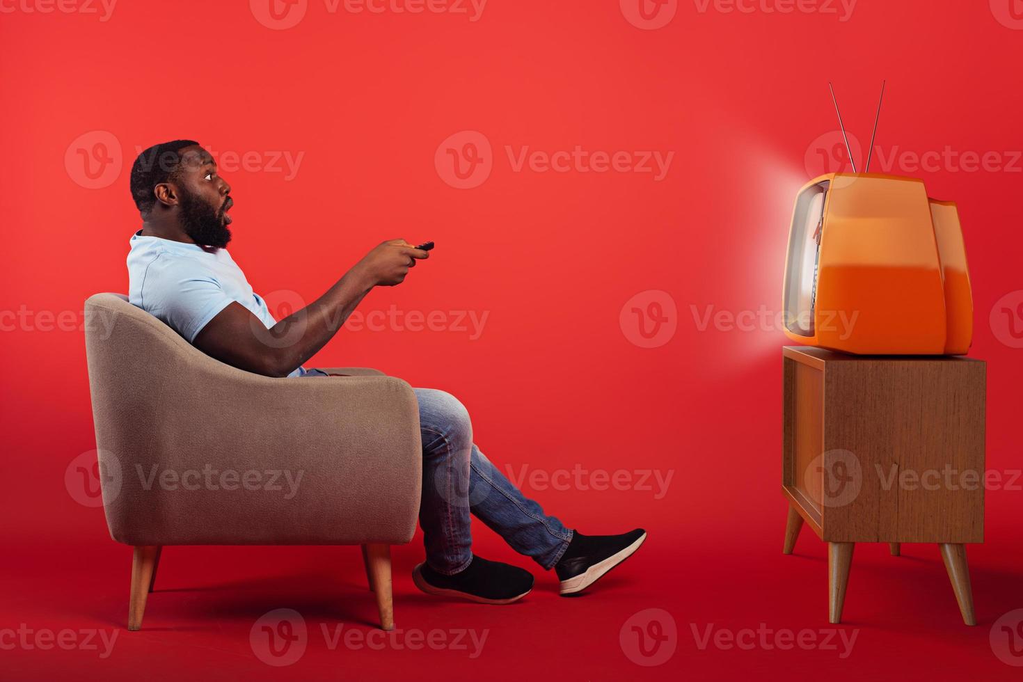 erstaunt Mann im das Sessel Uhren ein Film auf ein Jahrgang Fernseher auf rot Hintergrund foto