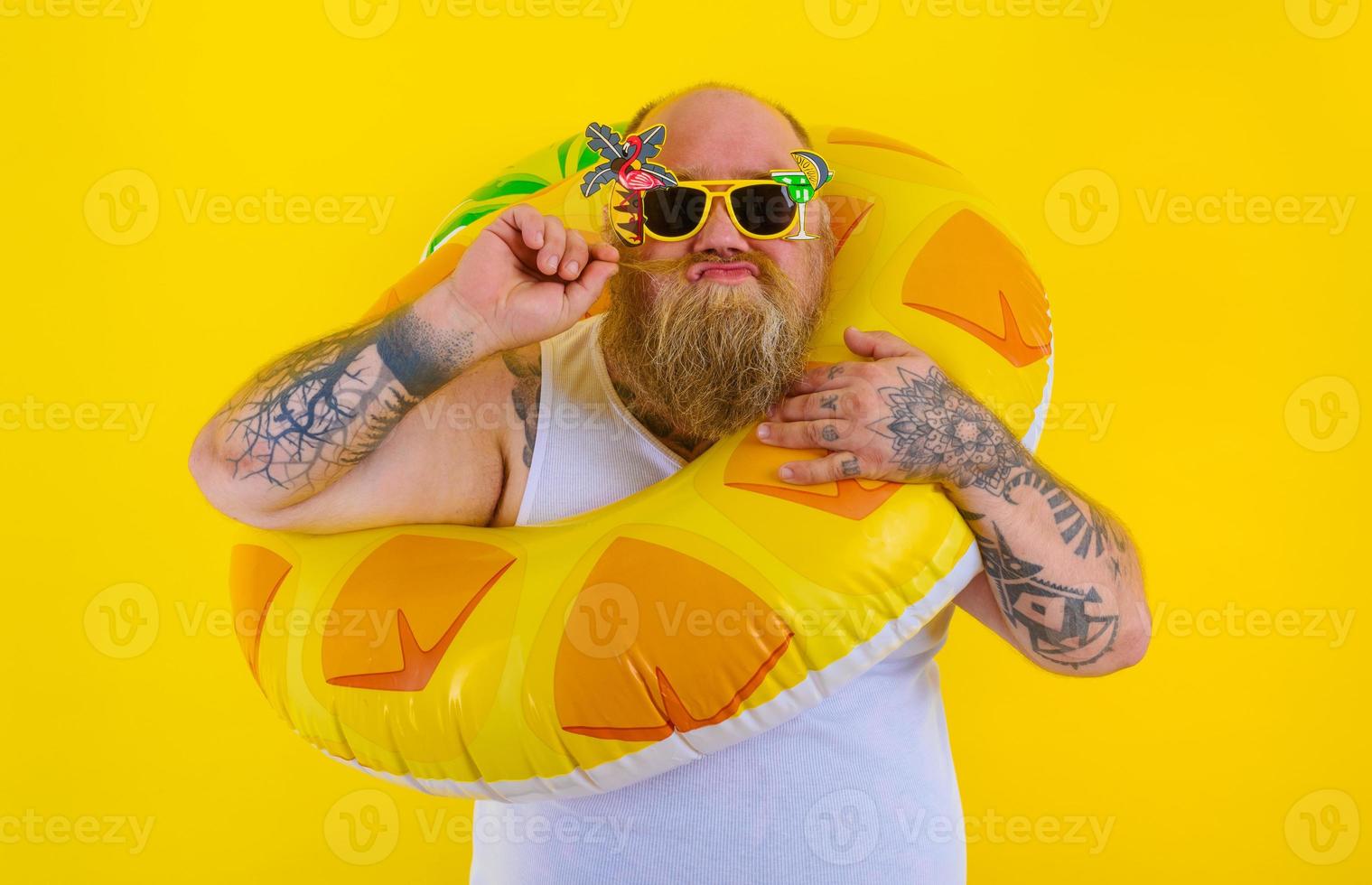 Fett nachdenklich Mann mit Perücke im Kopf ist bereit zu schwimmen mit ein Krapfen Lebensretter foto