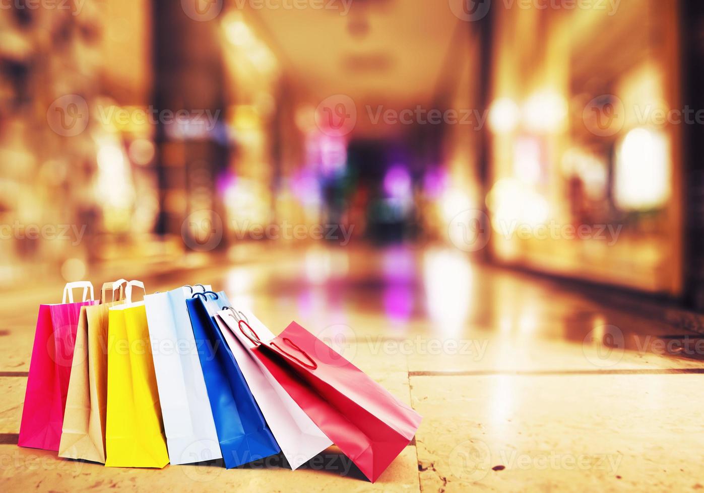 bunt Einkaufen Taschen auf das Boden mit ein Galerie von luxuriös Geschäfte im das Hintergrund foto