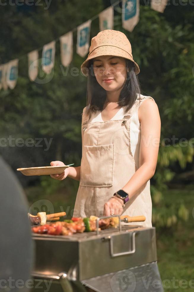 jung asiatisch Frau Grillen Grill Spieße Fleisch auf Grill Grill im Hinterhof auf Picknick Zeit foto