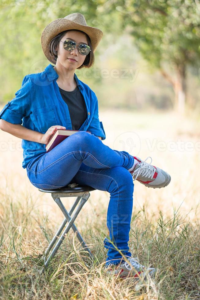 Frau trägt Hut und liest das Buch auf dem Stuhl foto