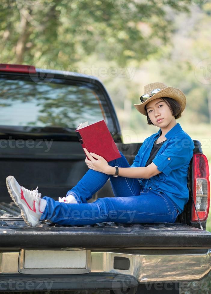 Frau trägt Hut und liest das Buch auf Pickup-Truck foto