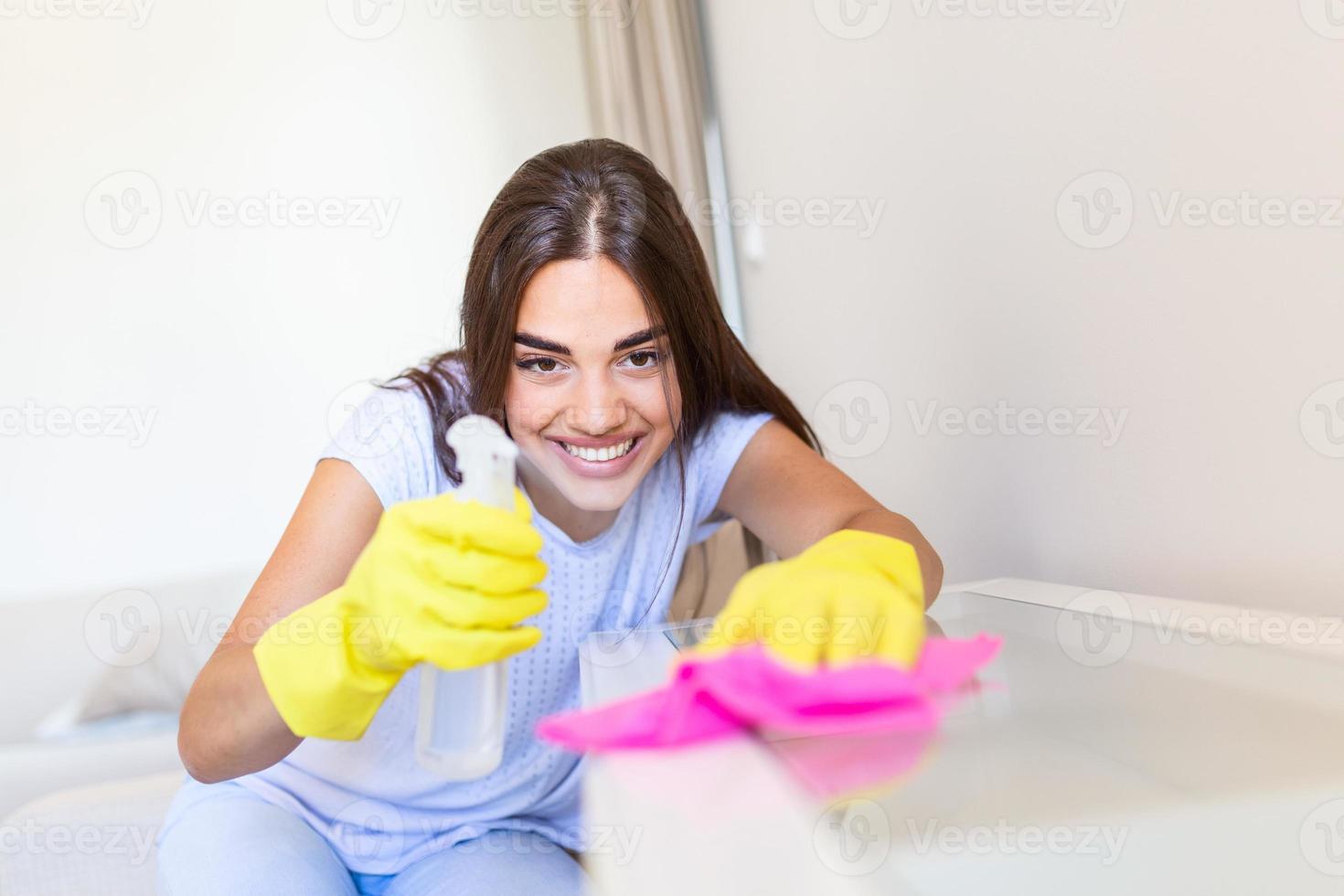 schön jung Frau macht Reinigung das Haus. Mädchen reibt Staub. lächelnd Frau tragen Gummi schützend Gelb Handschuhe Reinigung mit Lappen und sprühen Flasche Waschmittel. heim, Hauswirtschaft Konzept. foto