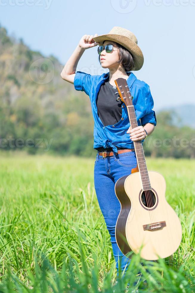 Frau trägt Hut und trägt ihre Gitarre auf der Wiese foto