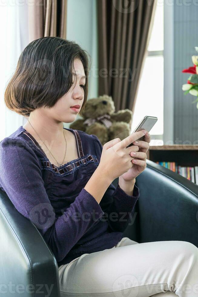 junge asiatische frau mit kurzen haaren benutzt handy im wohnzimmer foto