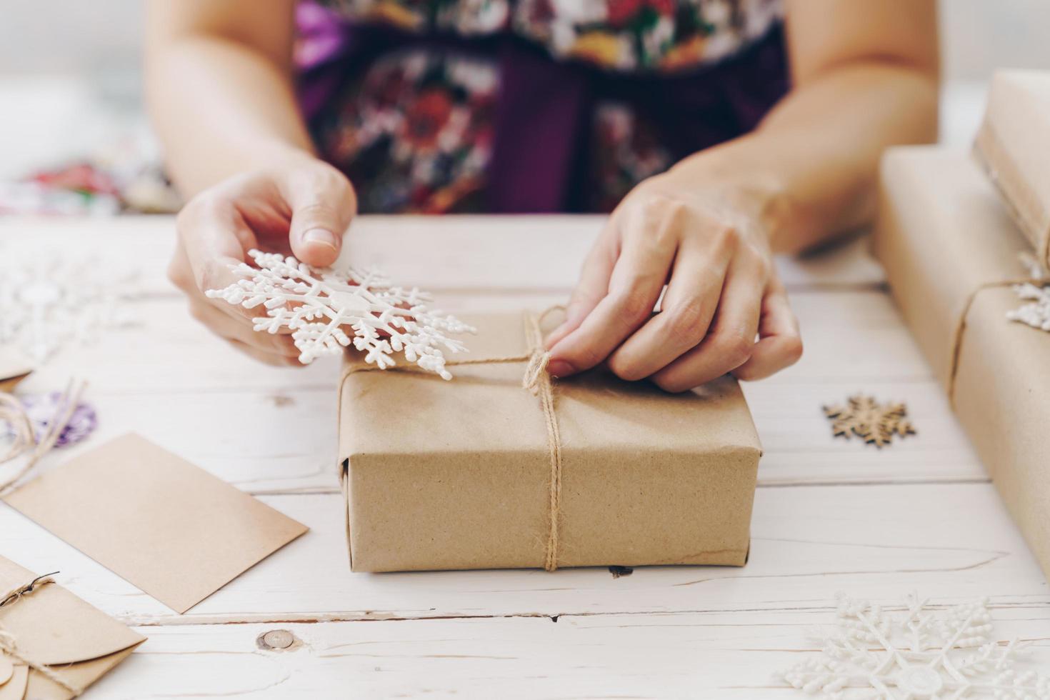 schließen oben von Hände halten Verpackung Geschenk Box auf hölzern Tabelle mit Weihnachten Dekoration. foto