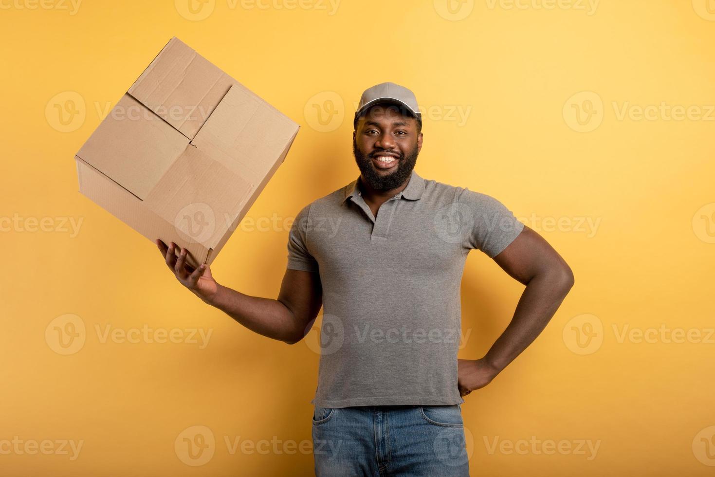 glücklich Kurier mit ein Box zu liefern. emotional Ausdruck. Gelb Hintergrund foto