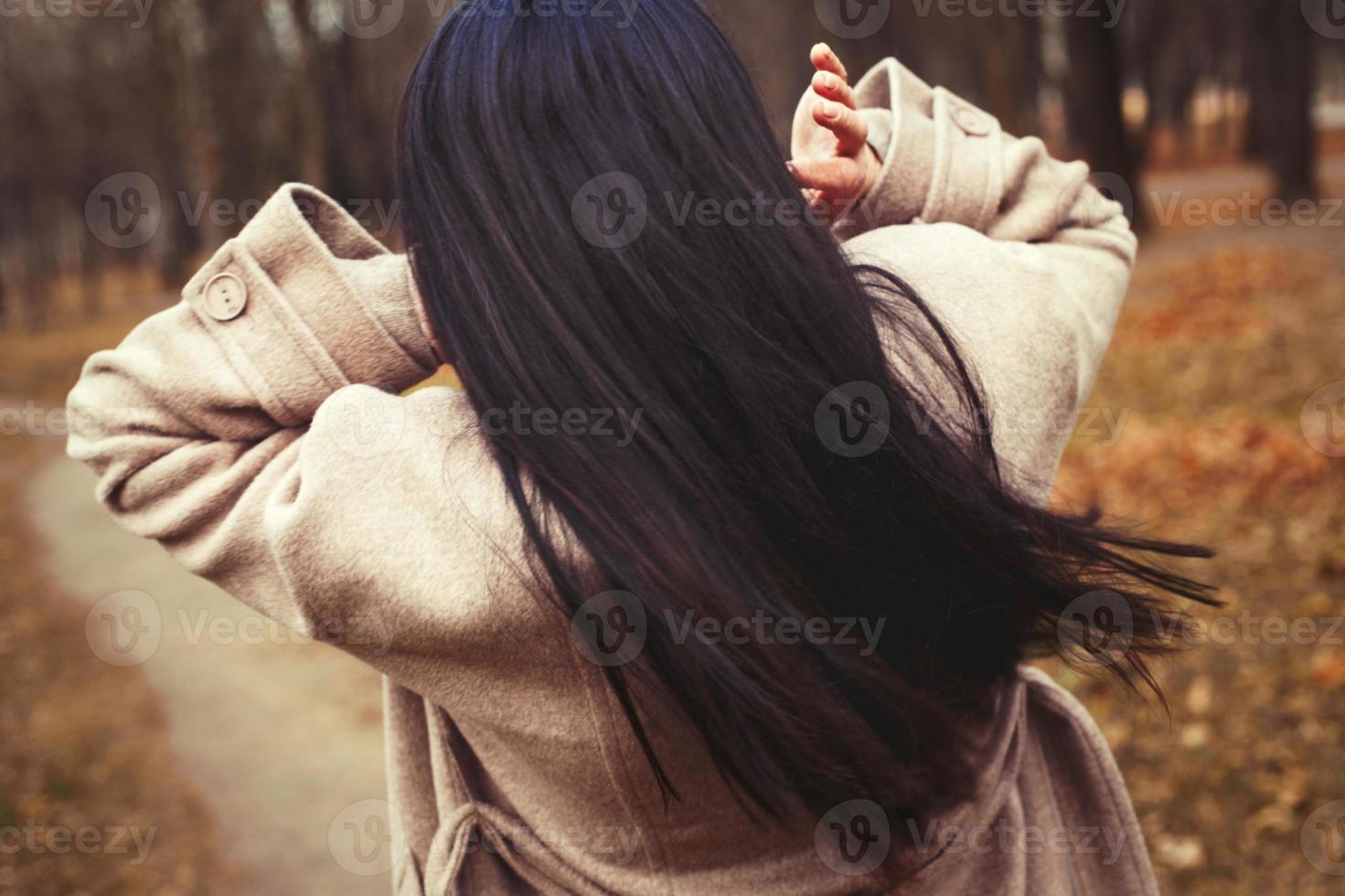 Porträt von Brünette Haar Frau im Beige Mantel Gehen beim das Stadt Park . foto