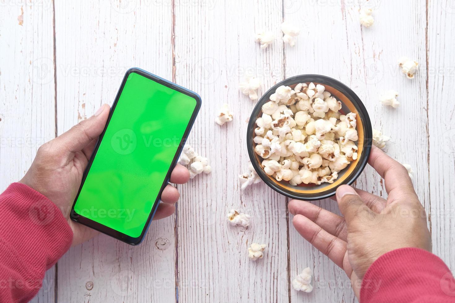 Mann mit Smartphone und Popcorn essen foto