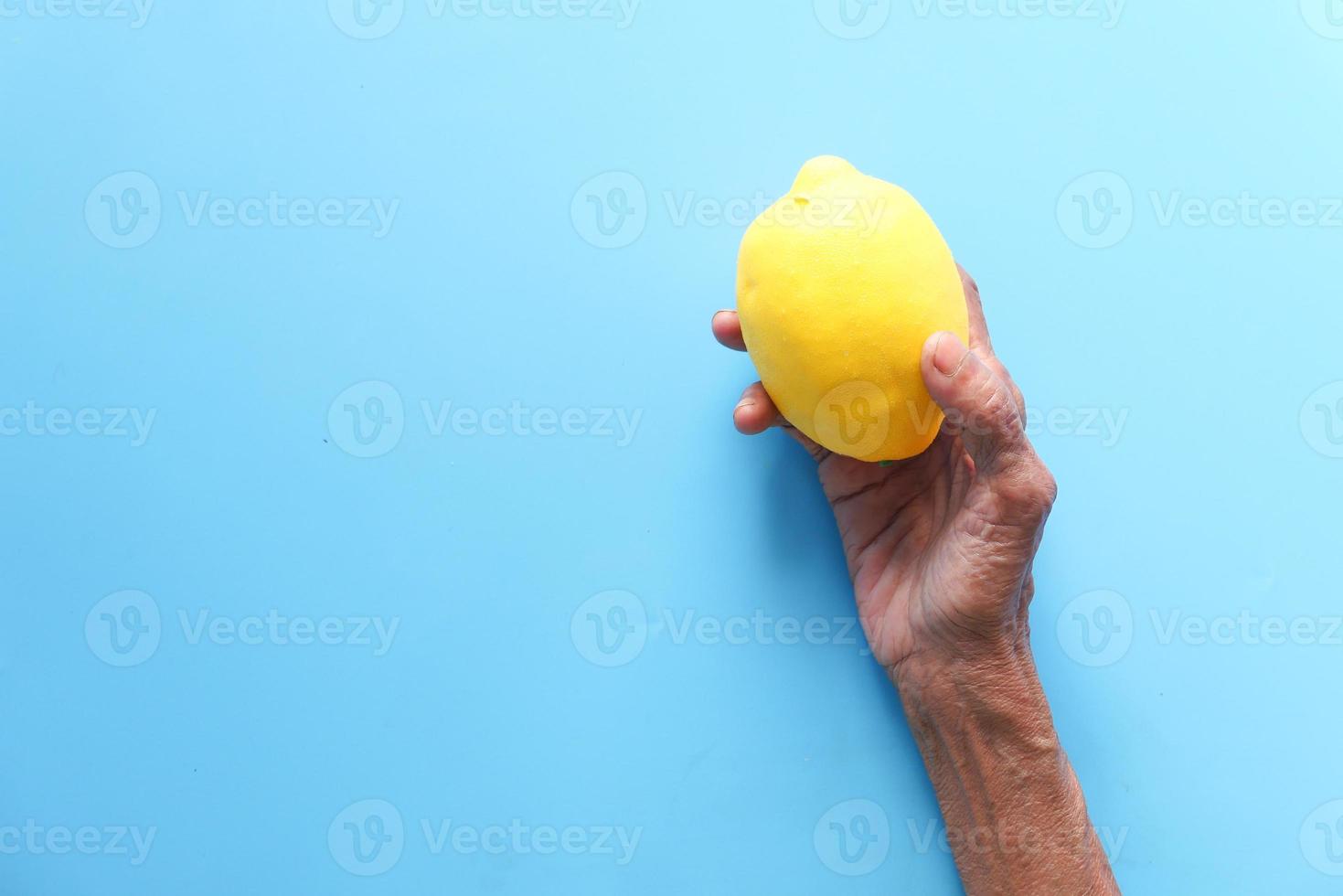 alte Frau, die Zitrone auf blauem Hintergrund hält foto
