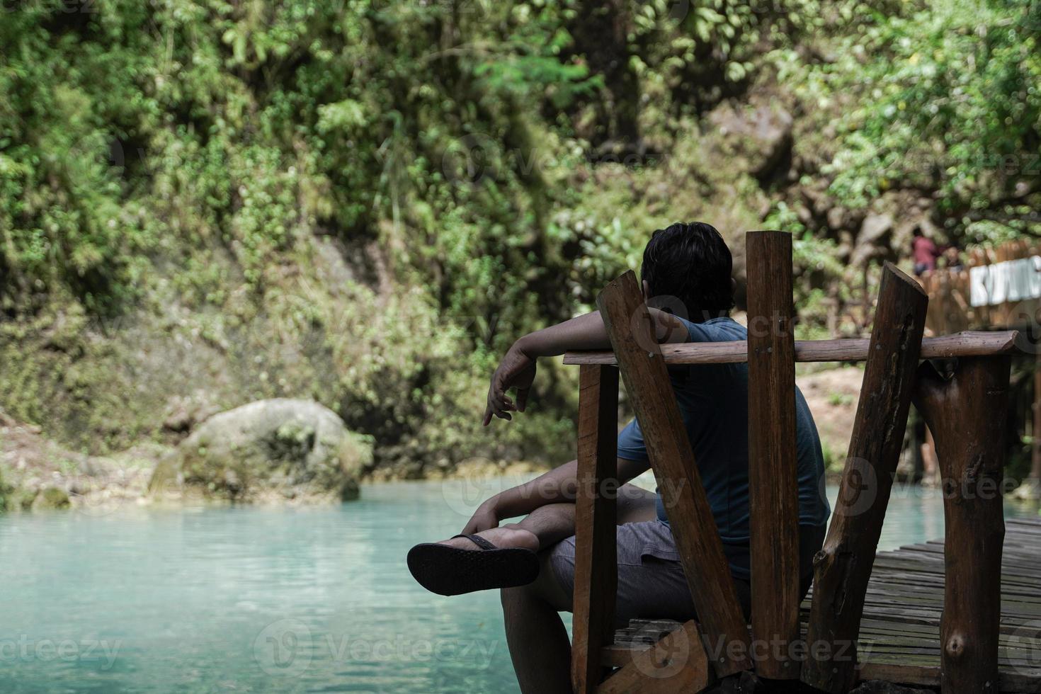 ein Mann Sitzung entspannt auf das Kante von ein Fluss wo das Wasser ist ruhig, ist beim das kedung pedut Tourist Stelle. foto