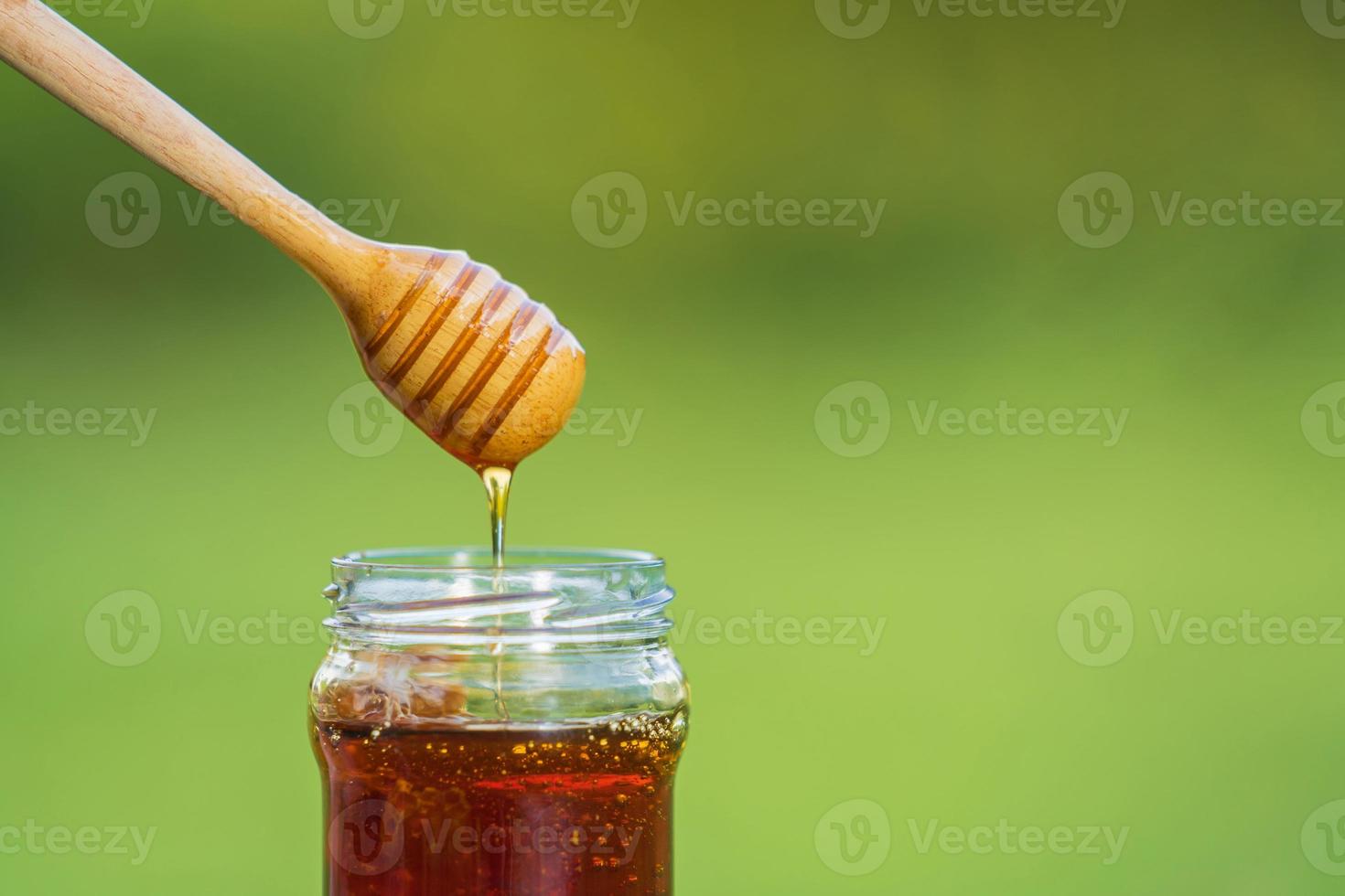 Honig tropft von Honigschöpflöffel auf natürlichem grünem Hintergrund foto