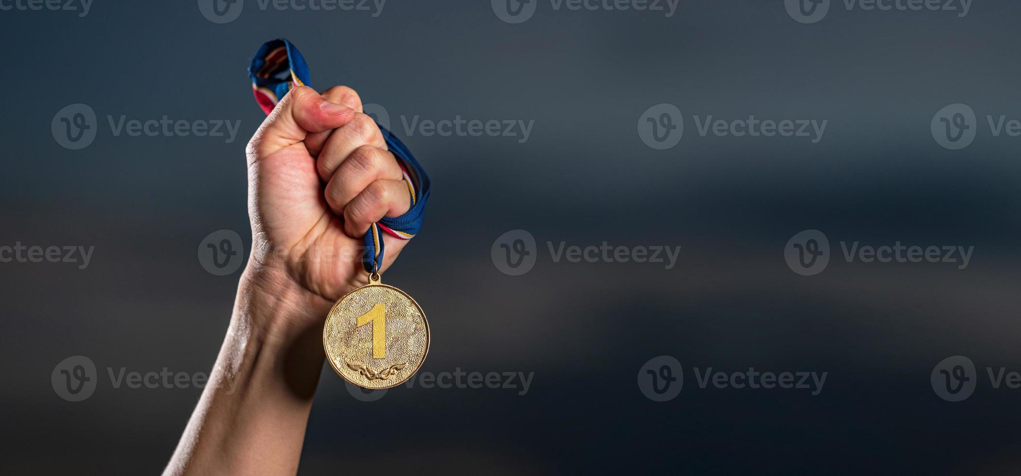 Hand, die Goldmedaille gegen wolkigen Zwielichthimmelhintergrund hält foto