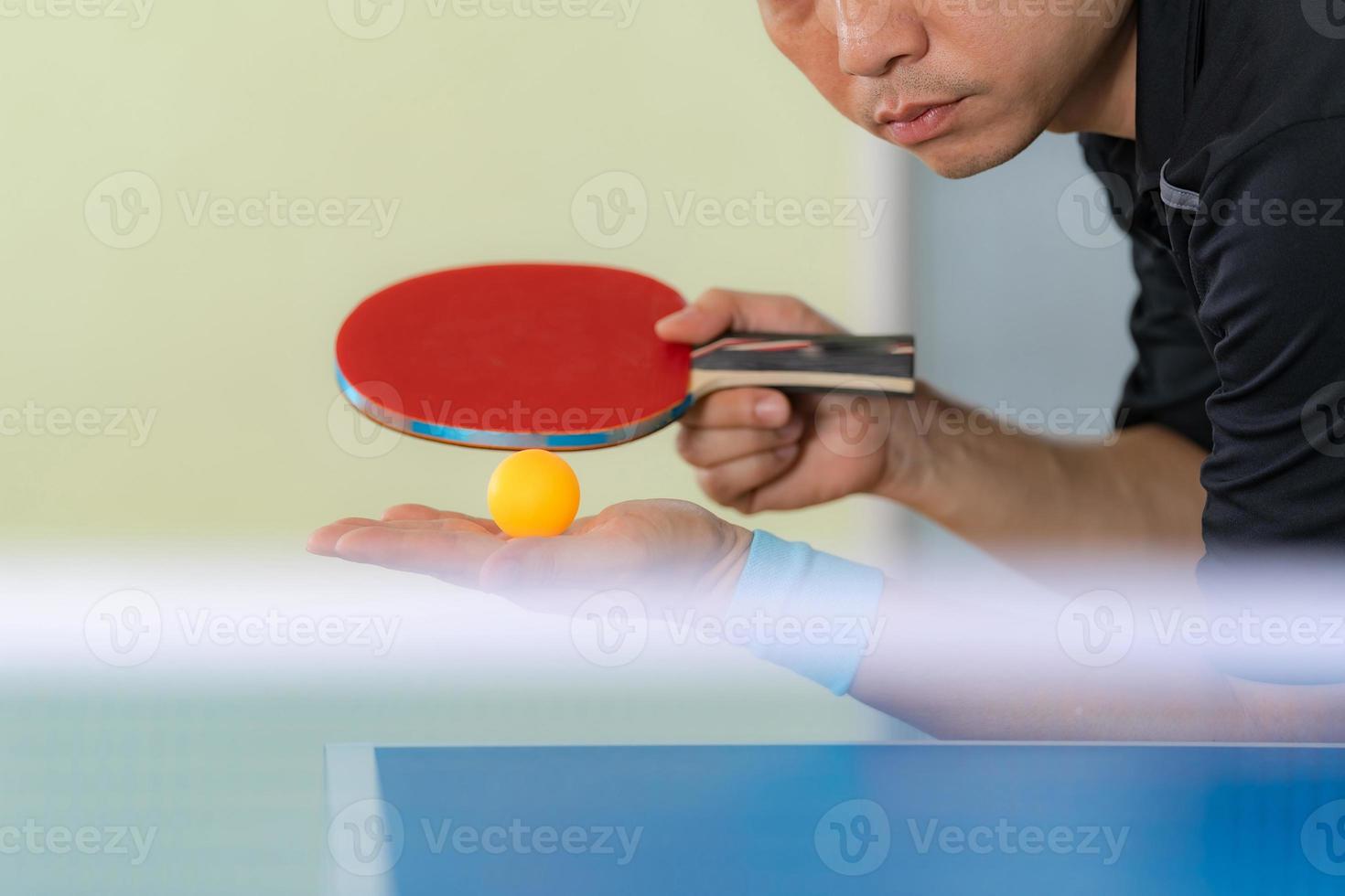 Mann, der Tischtennis mit Schläger und Ball in einer Sporthalle spielt foto