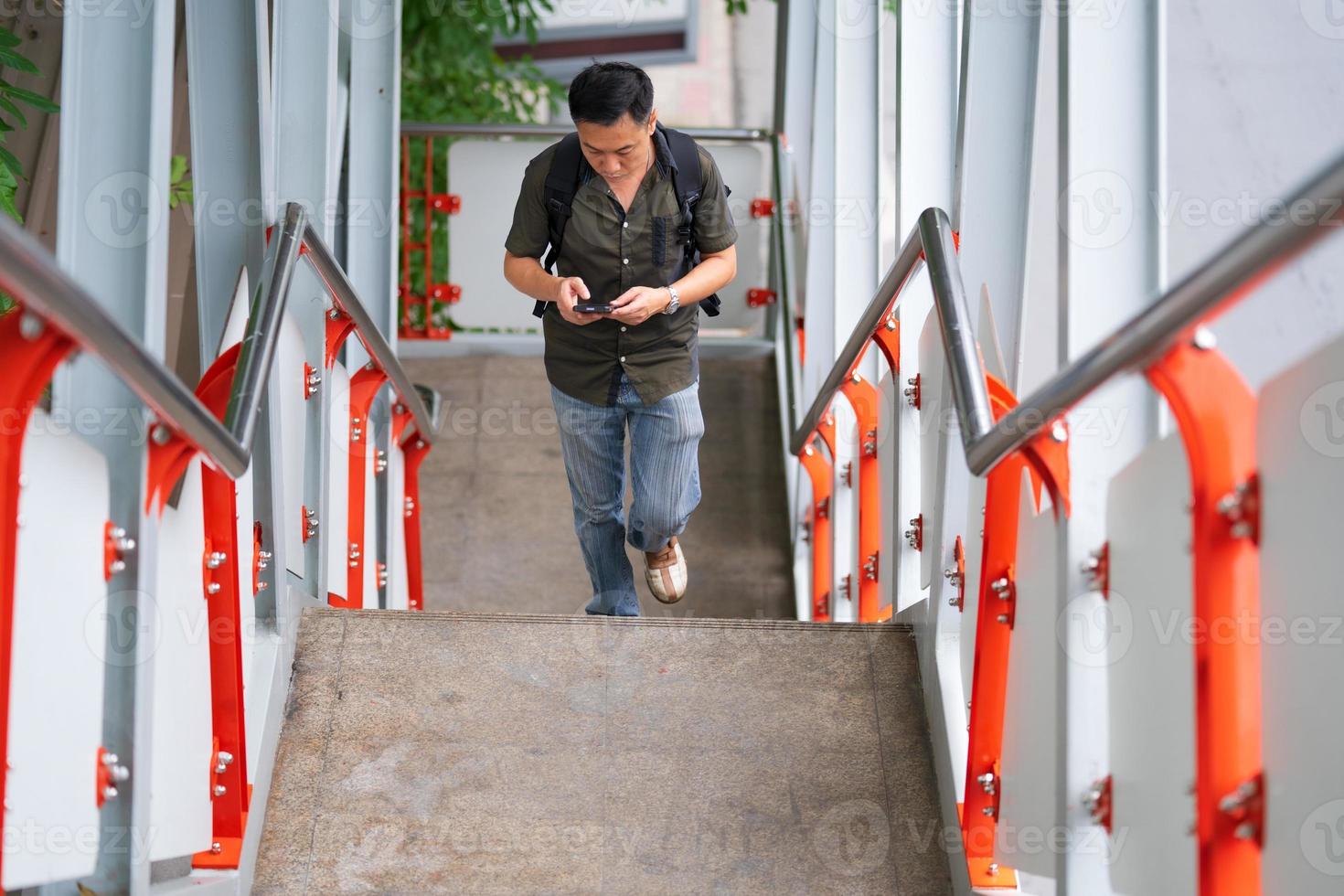 Mann, der Treppe hinaufgeht und Smartphone in der Stadt benutzt foto